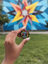 Glossy black pinback button with floral art and bold white text that reads “Hands Off My Body.” Feminist political button featuring bright pastel flowers in pink, red, orange, and yellow. Metal pin with durable safety pin back, shown in various settings: held by hand, displayed on pedestal, and against colorful street art. Available in 2" and 3" sizes, perfect for backpacks, jackets, tote bags, or as a gift for feminist allies and book lovers.